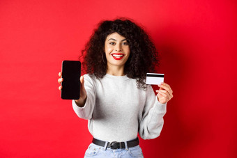 快乐好看的女孩显示塑料信贷卡空智能手机屏幕演示账户应用程序站红色的背景