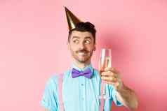 假期庆祝活动概念快乐的年轻的男人。庆祝生日聚会，派对他思考演讲提高玻璃chamapgne烤面包粉红色的背景