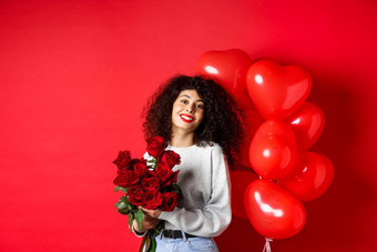假期庆祝活动快乐美丽的女人卷曲的头发收到花束玫瑰微笑站聚会，派对气球红色的背景
