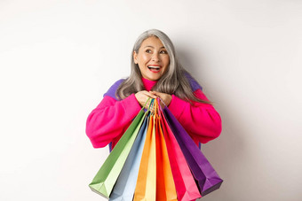 时尚高级亚洲女人购物狂拥抱购物袋微笑快乐的购买折扣站白色背景