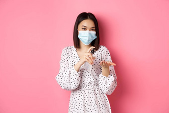 科维德流感大流行生活方式概念可爱的亚洲女人清洁手洗手液防腐剂穿医疗面具站粉红色的背景