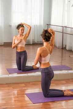 年轻的女人健身教练紫罗兰色的运动服装紧身裤前伸展运动健身房普拉提瑜伽席大镜子阳光明媚的一天女健身瑜伽例程概念
