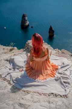 女孩红色的头发坐在回来查看器野餐毯子橙色衣服峰会山背景海岩石海