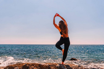 女人使心手海滩年轻的女人长头发健身教练伸展运动普拉提瑜伽席海阳光明媚的一天女健身瑜伽例程概念