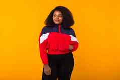 有趣的卷曲的非洲美国女孩穿着红色的体育夹克工作室黄色的背景Copyspace时尚人概念