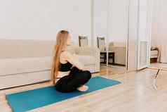 年轻的女人长头发健身教练黑色的运动服装伸展运动普拉提瑜伽席首页女健身瑜伽例程概念健康的生活方式和谐冥想