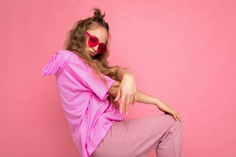 迷人的积极的年轻的金发女郎卷曲的女人孤立的粉红色的背景墙穿休闲粉红色的t恤时尚的色彩鲜艳的太阳镜相机跳舞