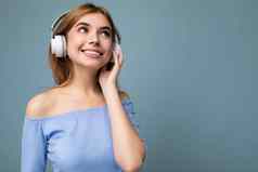 照片美丽的积极的微笑年轻的金发女郎女人穿蓝色的作物前孤立的蓝色的背景墙穿白色无线蓝牙耳机听很酷的音乐享受一边