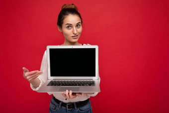 特写镜头肖像美丽的微笑快乐年轻的女人持有电脑移动PC相机指出显示穿休闲聪明的衣服孤立的红色的墙背景