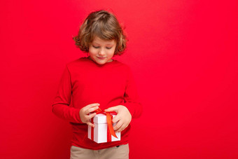 快乐金发女郎卷曲的男孩孤立的红色的背景墙穿红色的毛衣持有礼物盒子现在盒子