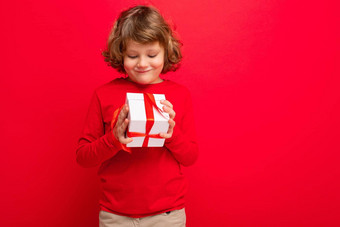 积极的金发女郎卷曲的男孩孤立的红色的背景墙穿红色的毛衣持有礼物盒子惊喜盒子