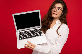 神秘的深思<strong>熟</strong>虑的美丽的<strong>褐色</strong>卷曲的年轻的女人持有电脑移动PC穿眼镜白色衬衫孤立的红色的墙背景