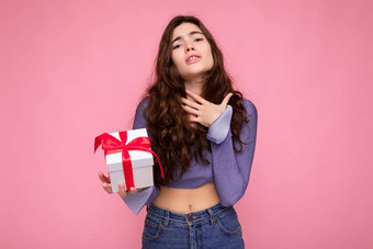 拍摄美丽的快乐惊讶褐色卷曲的年轻的女人孤立的粉红色的背景墙穿紫色的上衣持有白色礼物盒子红色的丝带相机
