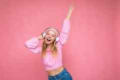 照片有吸引力的积极的微笑年轻的金发女郎女人穿粉红色的上衣粉红色的他孤立的粉红色的背景墙穿白色无线蓝牙耳机听音乐有趣的