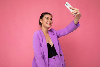 照片漂亮的年轻的女人穿紫色的西装采取<strong>自拍</strong>照片移动电话孤立的粉红色的<strong>背景</strong>电话相机