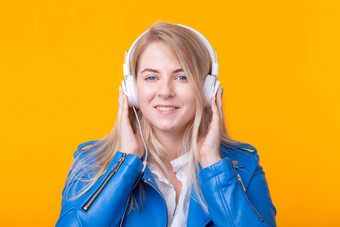 肖像可爱的积极的年轻的金发女郎女孩听最喜欢的音乐耳机蓝色的皮革夹克摆姿势黄色的背景概念音乐音乐会在线广播Copyspace