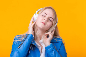 肖像可爱的积极的年轻的金发女郎女孩听最喜欢的音乐耳机蓝色的皮革夹克摆姿势黄色的背景概念音乐音乐会在线广播Copyspace