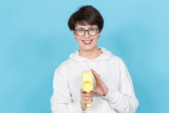 中年女人短发型毛衣眼镜持有黄色的古董电影相机蓝色的背景概念视频拍摄