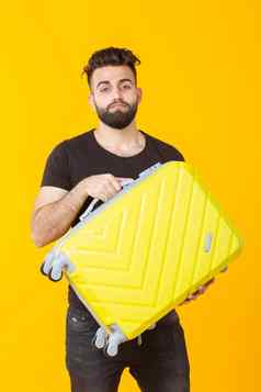 可爱的漂亮的年轻的阿拉伯男人。胡子持有黄色的手提箱手黄色的背景概念旅行假期