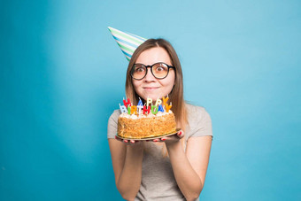 关闭有趣的积极的女孩眼镜问候纸他持有快乐生日蛋糕手站蓝色的背景