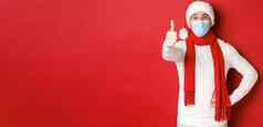 概念科维德圣诞节假期流感大流行快乐的英俊的男人。医疗面具圣诞老人他显示翘拇指庆祝一年社会距离