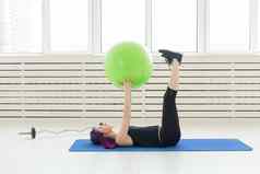 年轻的苗条的女孩锻炼伸展运动绿色健身球明亮的健身房健康的回来韧带概念