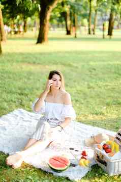 年轻的女人野餐格子坐着公园水果