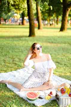 年轻的欧洲女孩太阳镜野餐格子坐着公园水果