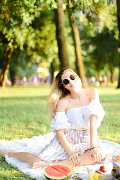 年轻的欧洲漂亮的女孩太阳镜野餐格子坐着公园水果