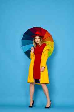 女人黄色的外套五彩缤纷的伞摆姿势蓝色的背景