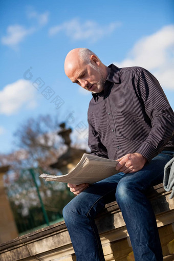 男人。坐着阅读报纸石头墙