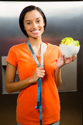 微笑浅黑肤色的女人磁带测量脖子持有碗沙拉