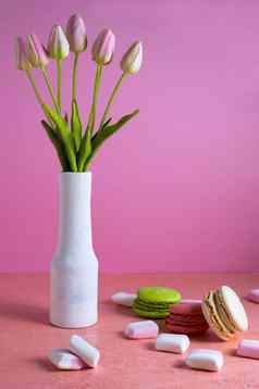 蛋白杏仁饼小白色粉红色的棉花糖分散苍白的粉红色的背景花瓶郁金香的地方文本
