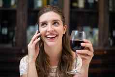 快乐的女人持有酒玻璃会说话的电话