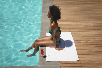 年轻的非洲美国女人坐着在游泳池边<strong>后院</strong>