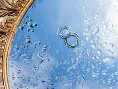 一对婚礼环湿镜子表面蓝色的天空反射关闭照片传统的珠宝新娘新郎