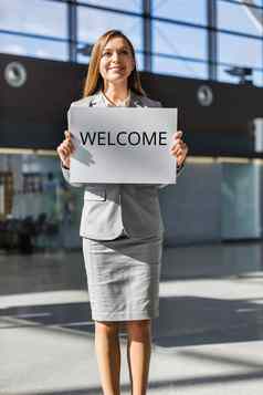 肖像女商人站持有白色董事会标志到来区域机场