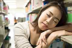 年轻的学生女孩睡觉累了阅读书图书馆