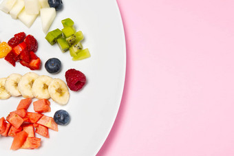 新鲜的水果沙拉白色板混合水果白色板健康的食物风格水果沙拉新鲜的水果浆果粉红色的背景