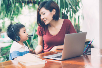 年轻的亚洲妈妈。儿子移动PC电脑研究学习首页男孩穿耳机电子学习距离老师妈妈支持孩子教育概念