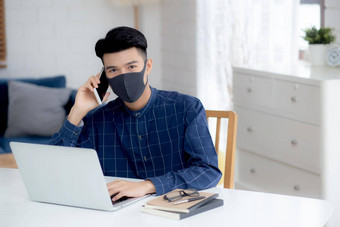 年轻的亚洲业务男人。脸面具会说话的智能手机工作移动PC电脑保护科维德商人检疫工作首页笔记本社会距离保持首页