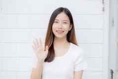 美丽的年轻的亚洲女人自信手势问候挥舞着手水泥背景首页友好的肖像女孩快乐的表达式快乐满意