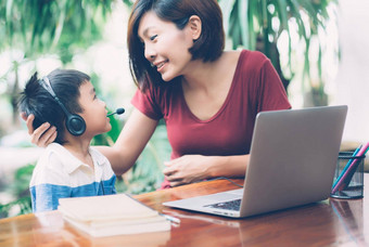 年轻的亚洲妈妈。儿子移动PC电脑研究学习首页男孩穿耳机电子学习距离老师妈妈支持孩子教育概念