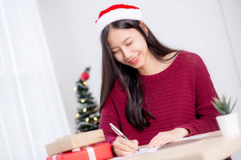 年轻的亚洲女人写作明信片圣诞节一天<strong>首页</strong>夏娃庆祝女写作消息问候卡给礼物盒子假期<strong>季</strong>节祝贺庆祝活动