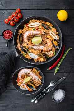 传统的西班牙语海鲜西班牙海鲜饭锅碗大米豌豆虾贻贝鱿鱼黑色的木木板前视图