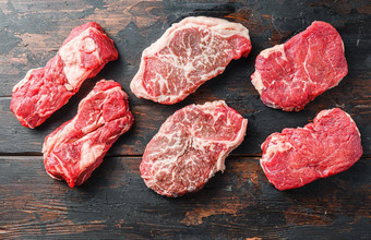 各种新鲜的黑色的安格斯主要的生牛肉steakes乡村黑暗木背景前视图