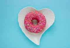 粉红色的甜蜜的甜甜圈坐在白色心形的板蓝色的背景