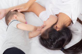 年轻的亚洲妈妈。触摸头婴儿女孩温柔的床上卧室妈妈爱新生儿护理女人表达式孩子父女儿家庭概念