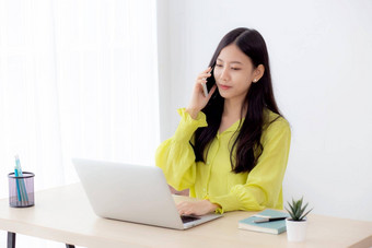 年轻的亚洲业务女人工作形式首页办公室调用电话成功首页女商人移动PC电脑桌子上女会说话的智能手机工作场所沟通概念