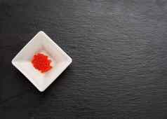 新鲜的粒度的红色的密友大马哈鱼鱼子酱白色陶瓷碗黑色的板岩石头背景